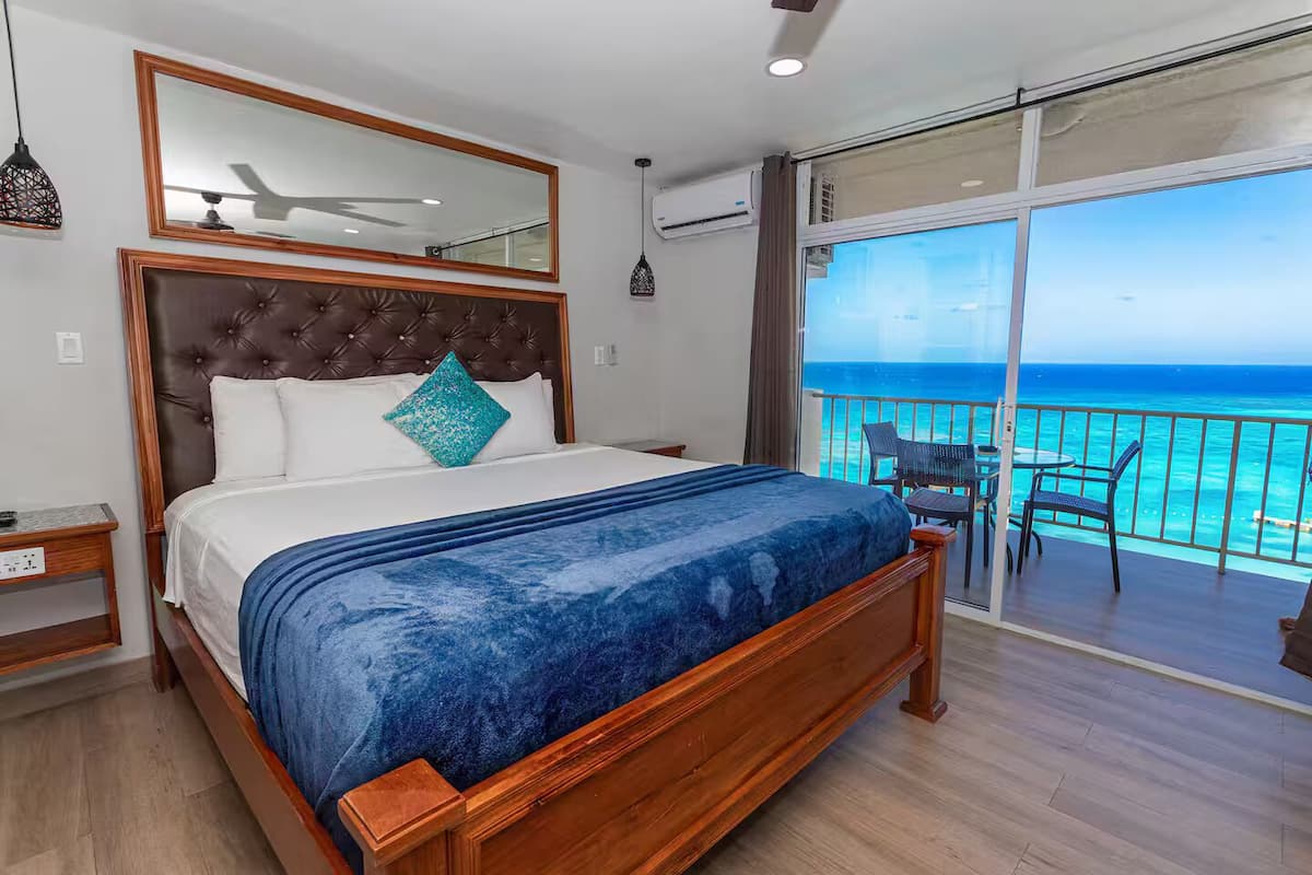 A bedroom with a large bed, a balcony with a view of the ocean, and a ceiling fan.
