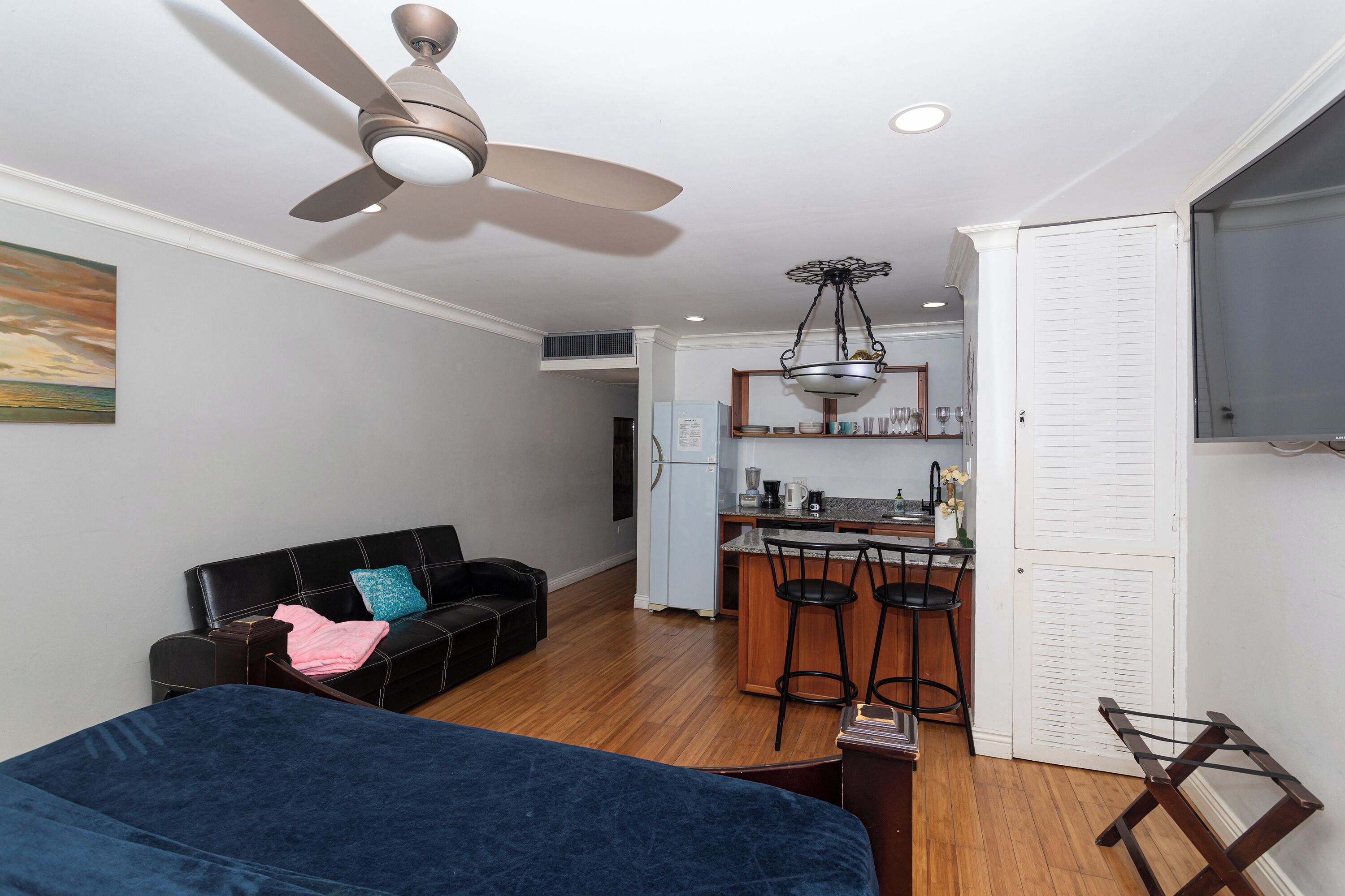 A compact living space with a kitchenette, a ceiling fan, a dining area with bar stools, and a bed.