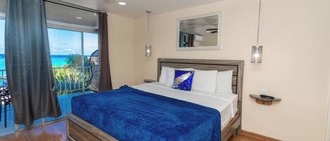 Een slaapkamer met een bed, een plafondventilator, uitzicht op de oceaan en een balkon met een stoel.