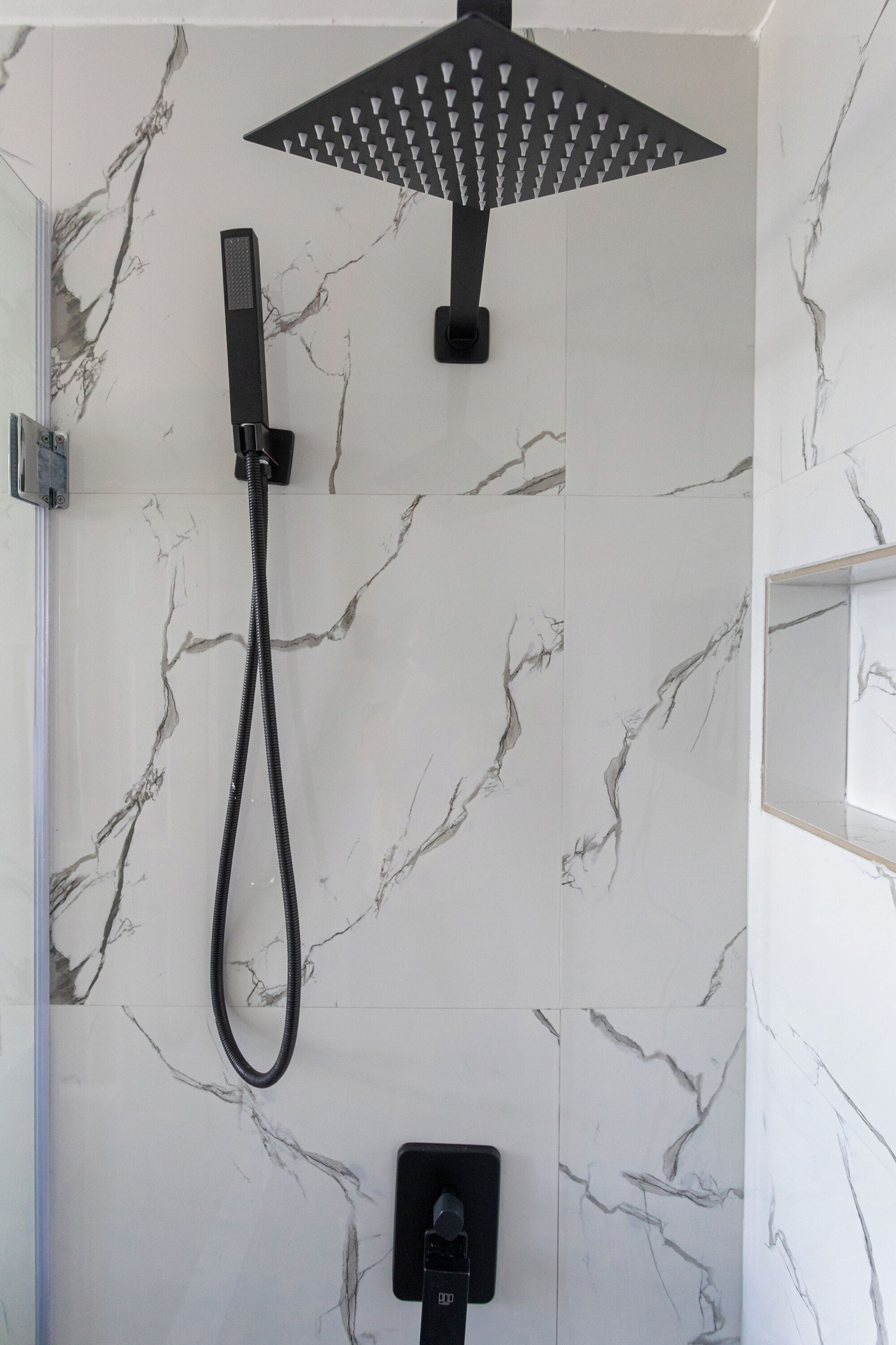 Una ducha moderna con un cabezal de ducha manual y un cabezal de ducha tipo lluvia, montada en una pared con diseño de mármol.