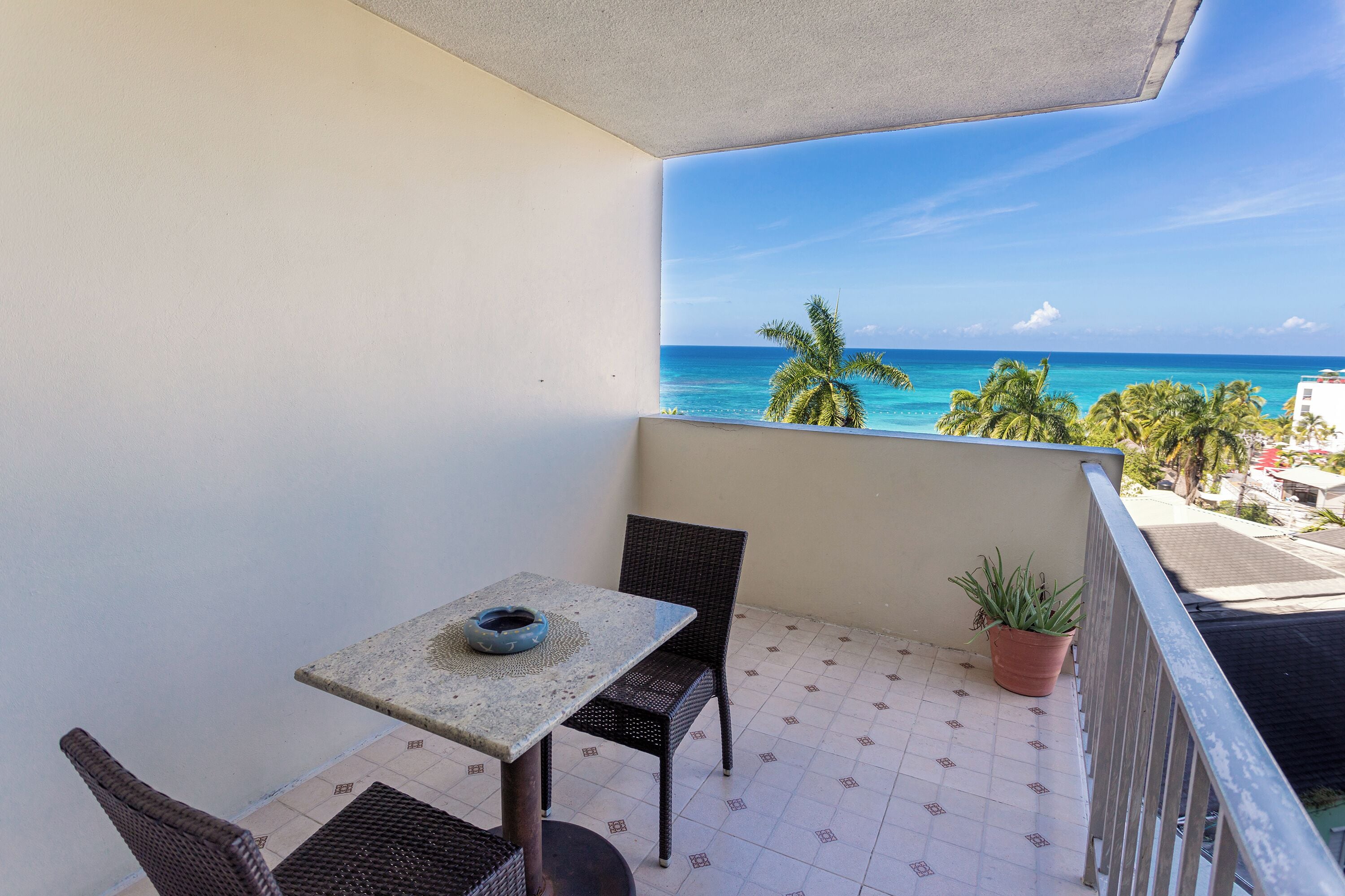 Uma varanda com mesa e cadeiras, um vaso com planta e vista para o mar.