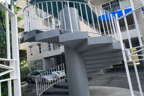 A multi-level building with a central staircase, balconies, and a car parked nearby. - Montego Bay Club Apartments (Montego Bay)