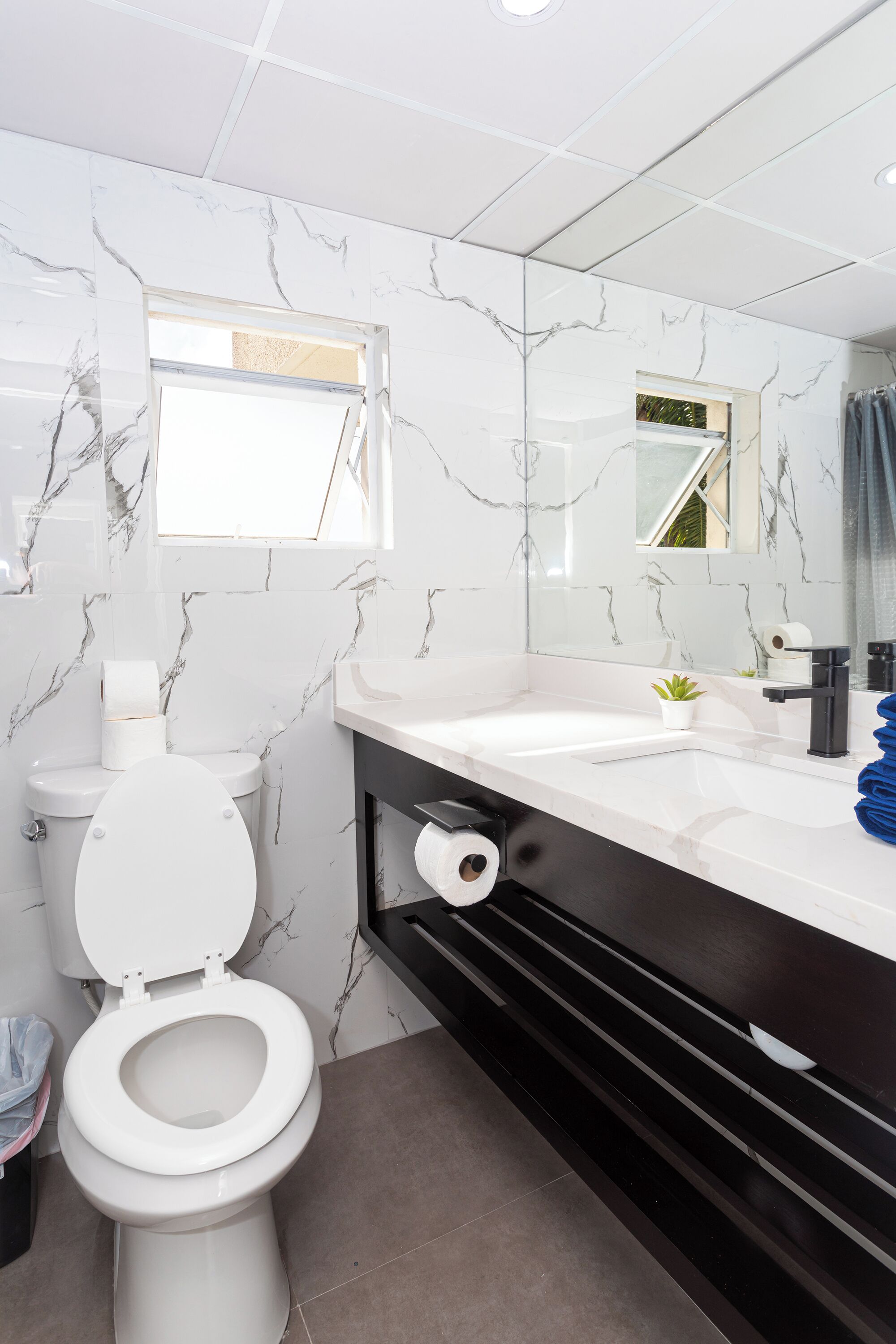 Ein modernes Badezimmer mit Toilette, Wänden im Marmoroptik, einem großen Spiegel und einem schwarzen Waschtisch.
