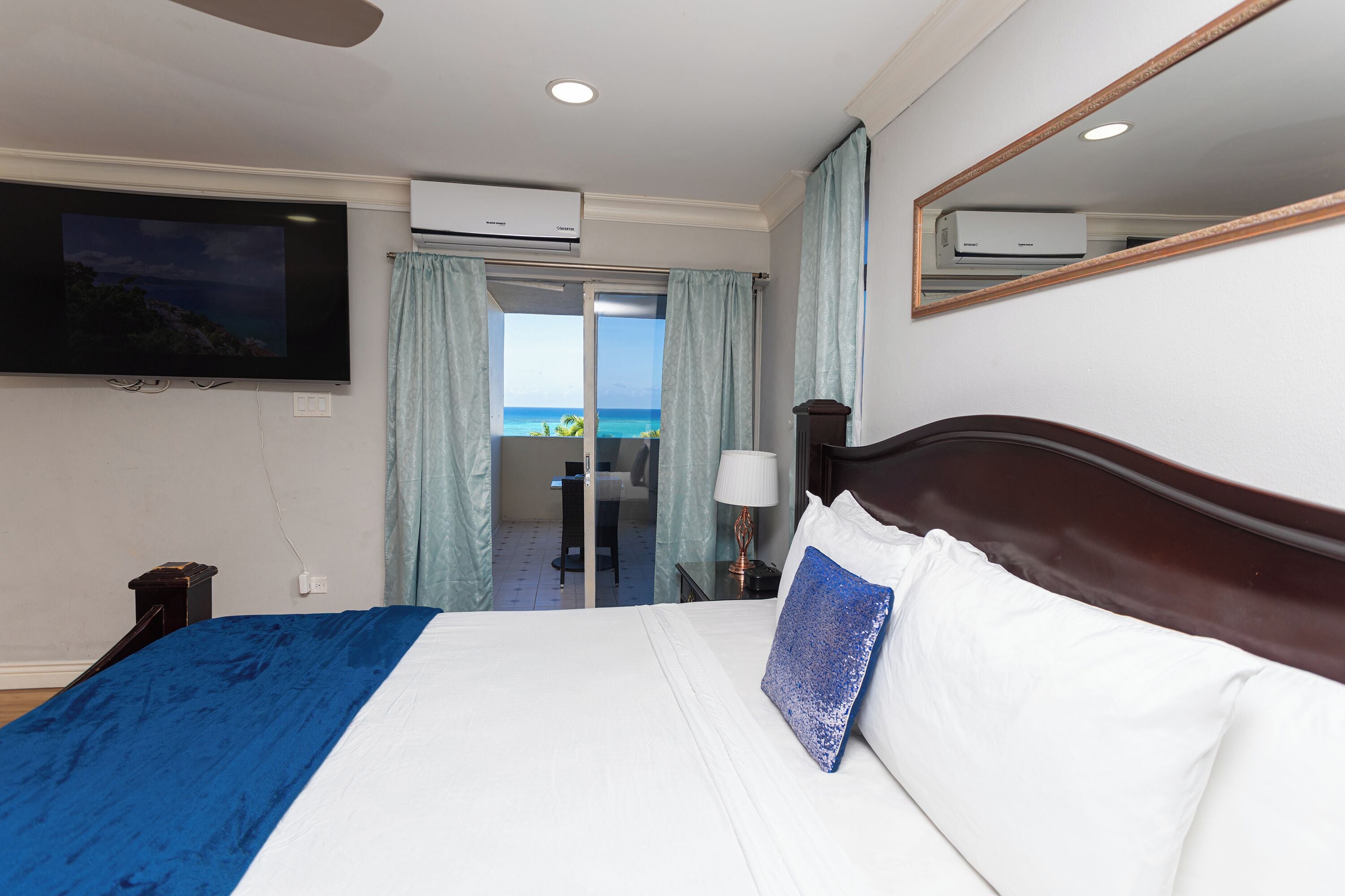 Quarto de hotel com cama, televisão na parede, aparelho de ar condicionado, janela com cortinas e vista para o mar.