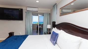 Quarto de hotel com cama, televisão na parede, aparelho de ar condicionado, janela com cortinas e vista para o mar.
