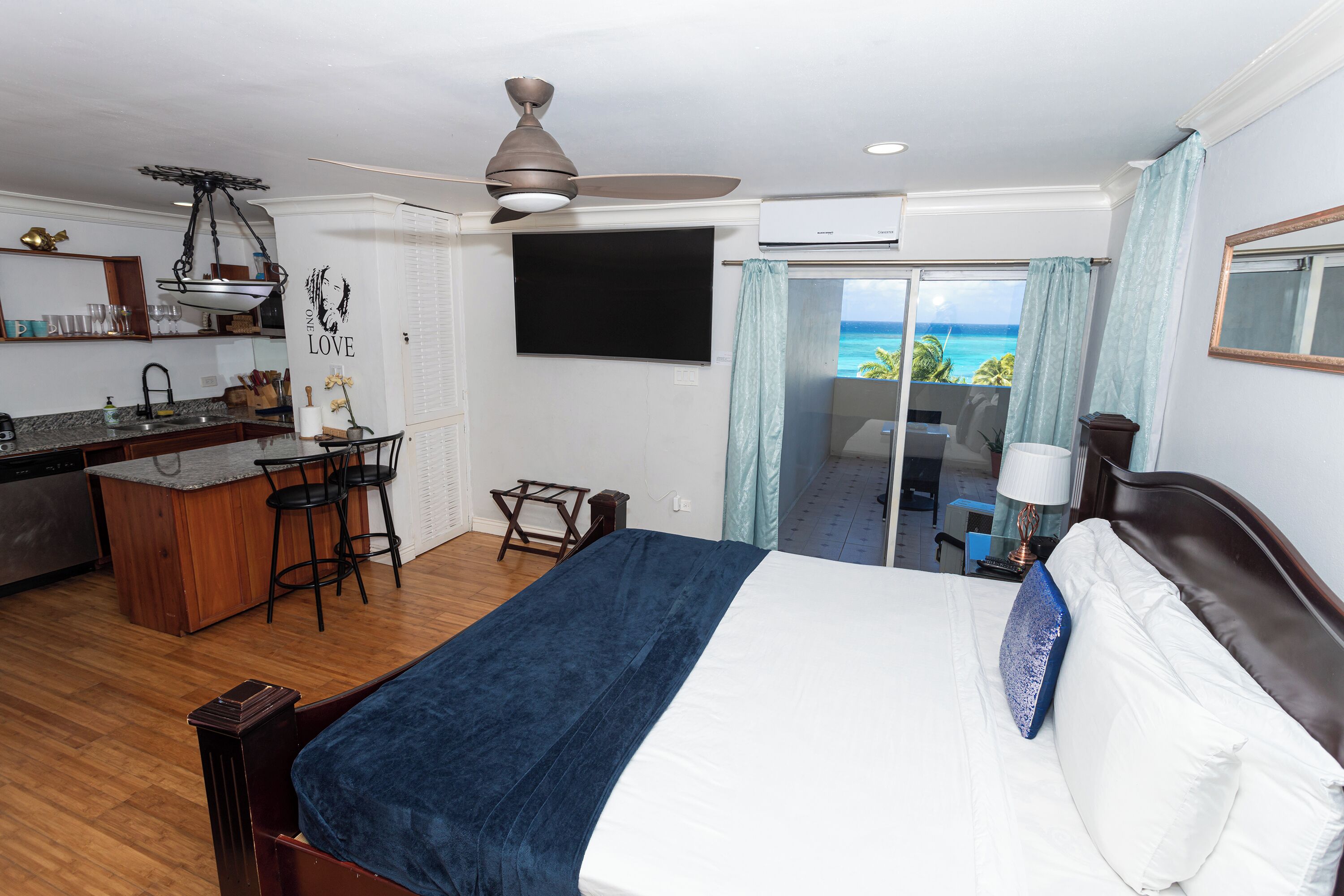 Une chambre d’hôtel équipée d’un lit, d’un bureau, d’une chaise, d’une télévision et d’un balcon avec vue sur l’océan.