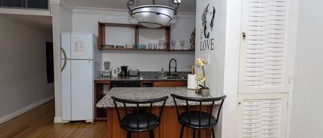 Una cucina con isola centrale, due sgabelli da bar, un frigorifero, un lavello e una lampada a sospensione.