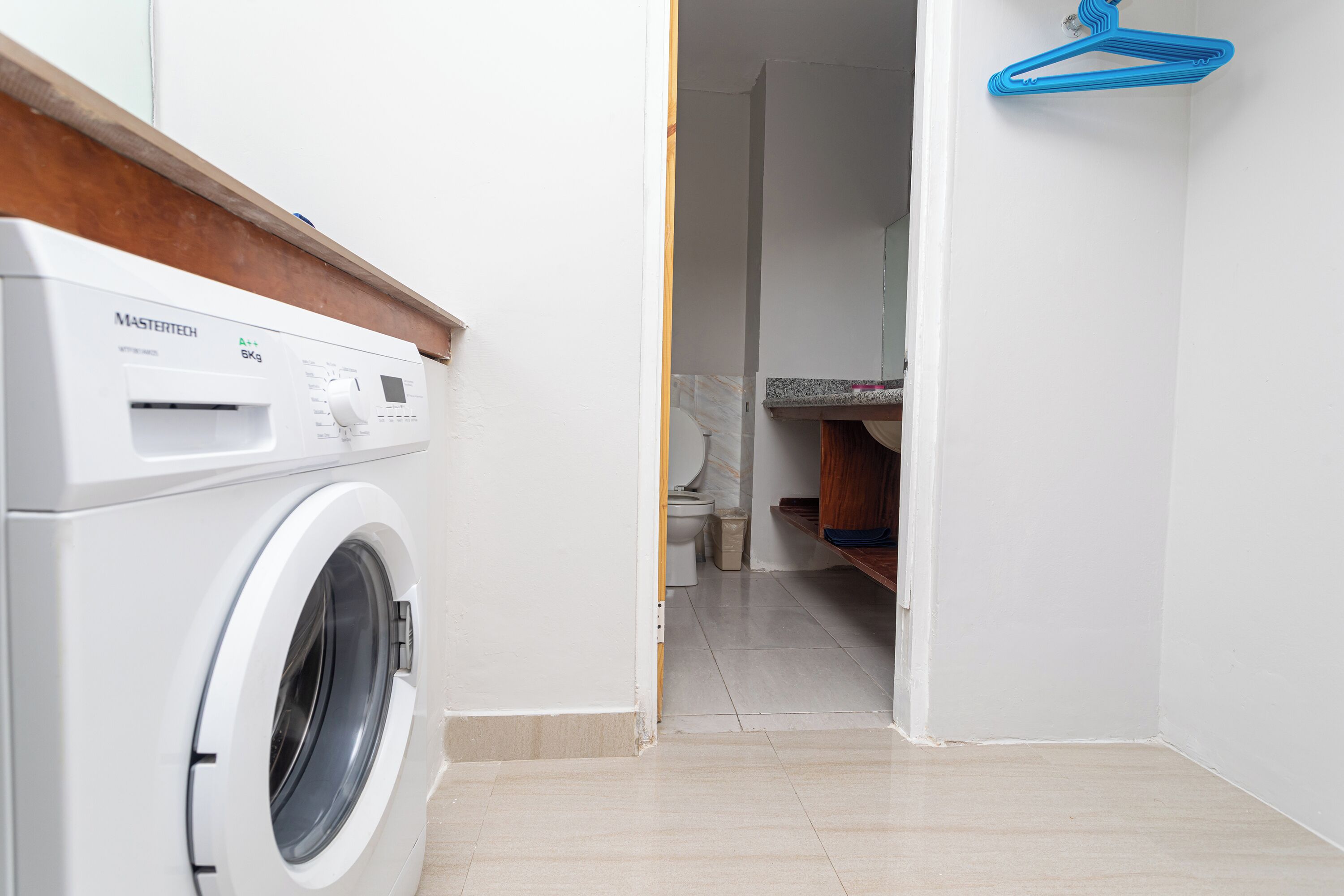 A laundry area with a white washing machine, a blue hanger, and a tiled floor.