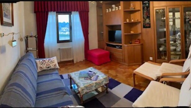 Ett kompakt vardagsrum med en soffa, ett litet bord, en röd pall, ett träskåp och en tv.