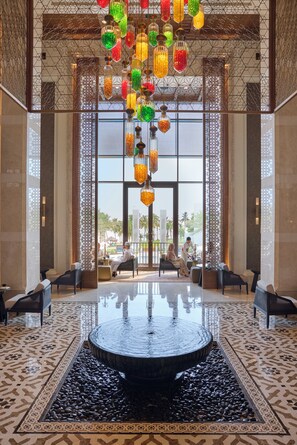 A lobby with a water feature, seating, and a view of palm trees.