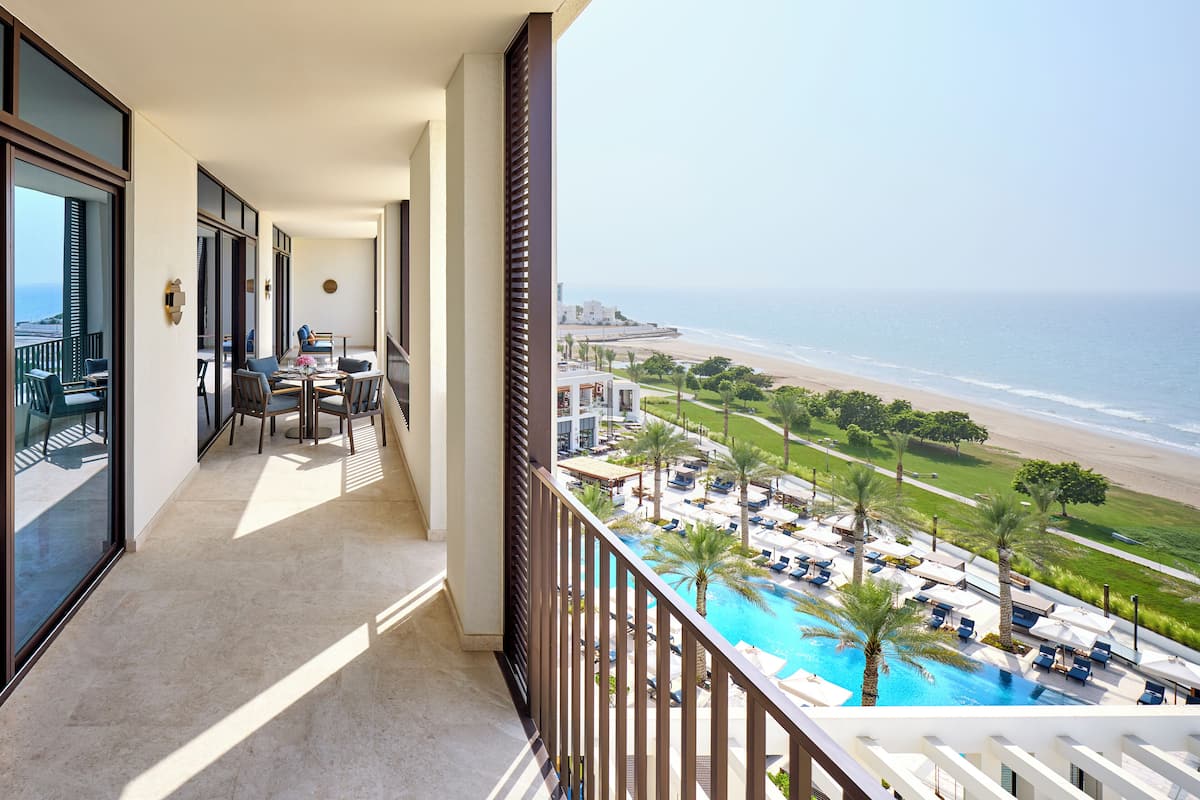 Un balcón con vistas a la playa, una zona de piscina con tumbonas y un comedor con mesa y sillas.