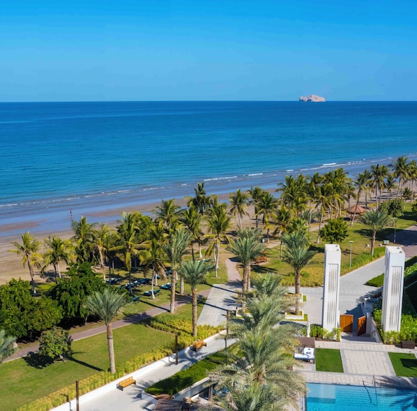 A resort with a pool, palm trees, and a view of the ocean.