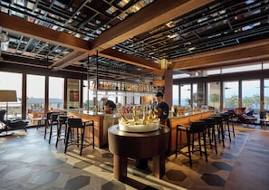 A bar area with a bartender, a large cake on a table, and a view of the ocean.
