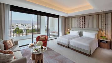 Una habitación de hotel moderna con una cama grande, un sofá, una mesa de comedor con un florero y vistas a la ciudad a través de amplias ventanas.