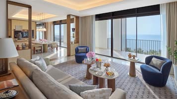 Una habitación de hotel moderna con sofá, sillones, una mesa de comedor y un balcón con vistas.