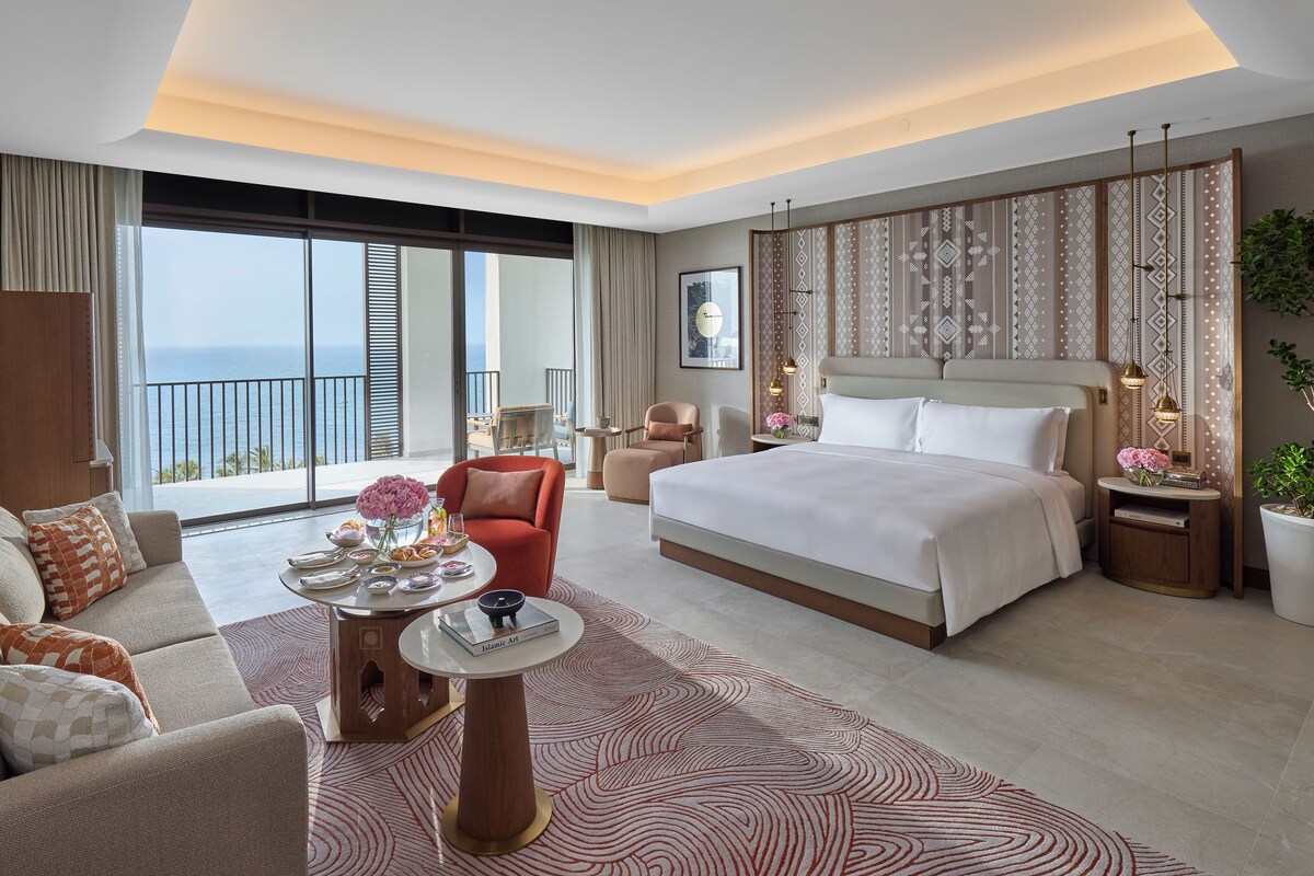 Une chambre d’hôtel moderne dotée d’un grand lit, d’un canapé, d’une table à manger et offrant une vue sur la mer.