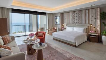 Habitación de hotel moderna con una cama grande, un sofá, una mesa de comedor y vistas al mar.