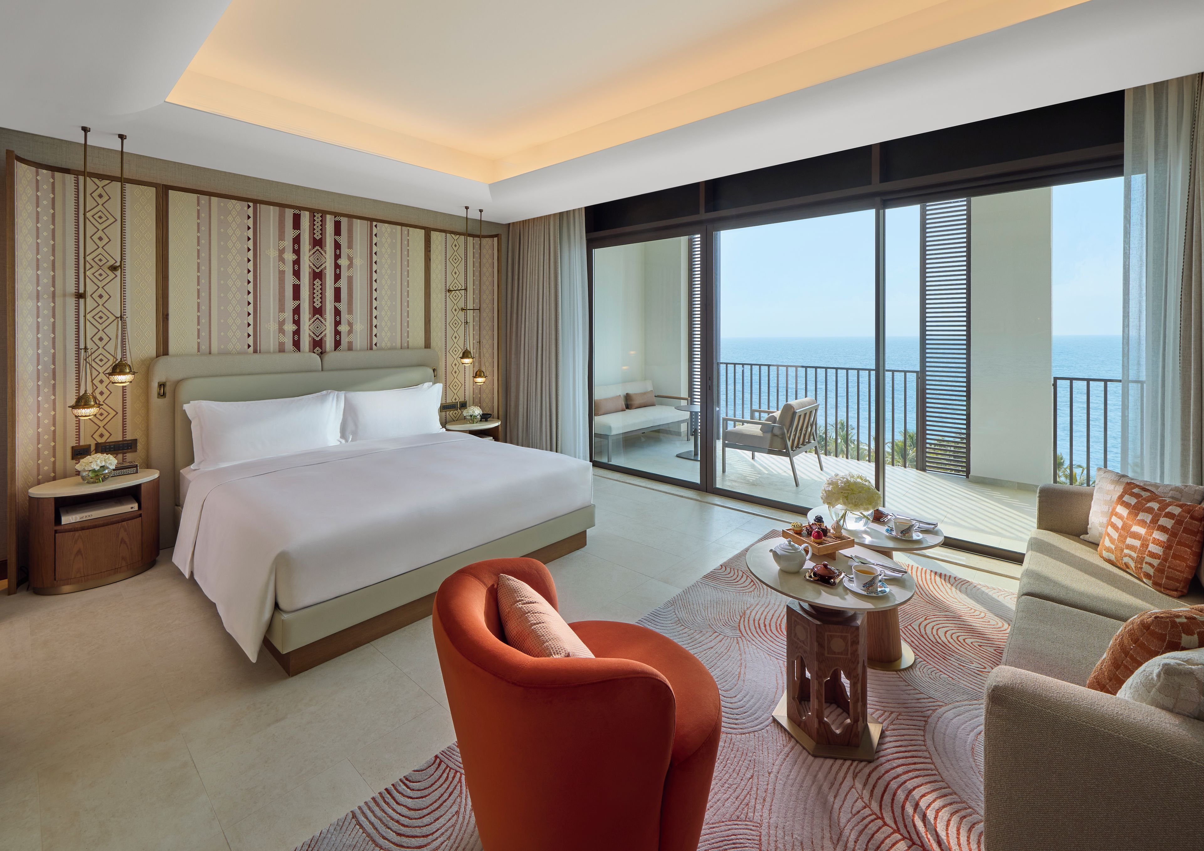 Habitación de hotel con una cama grande, un sofá, una mesa de comedor y un balcón con vista al mar.