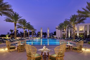 A poolside area with lounge chairs, a table with a drink, and palm trees. - Mandarin Oriental Muscat (Muscat)