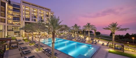 A hotel with a swimming pool, sun loungers, and palm trees.