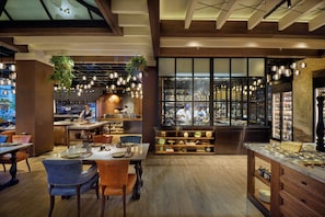 A restaurant interior with wooden floors, hanging plants, and a view of the kitchen through large windows. - Mandarin Oriental Muscat (Muscat)