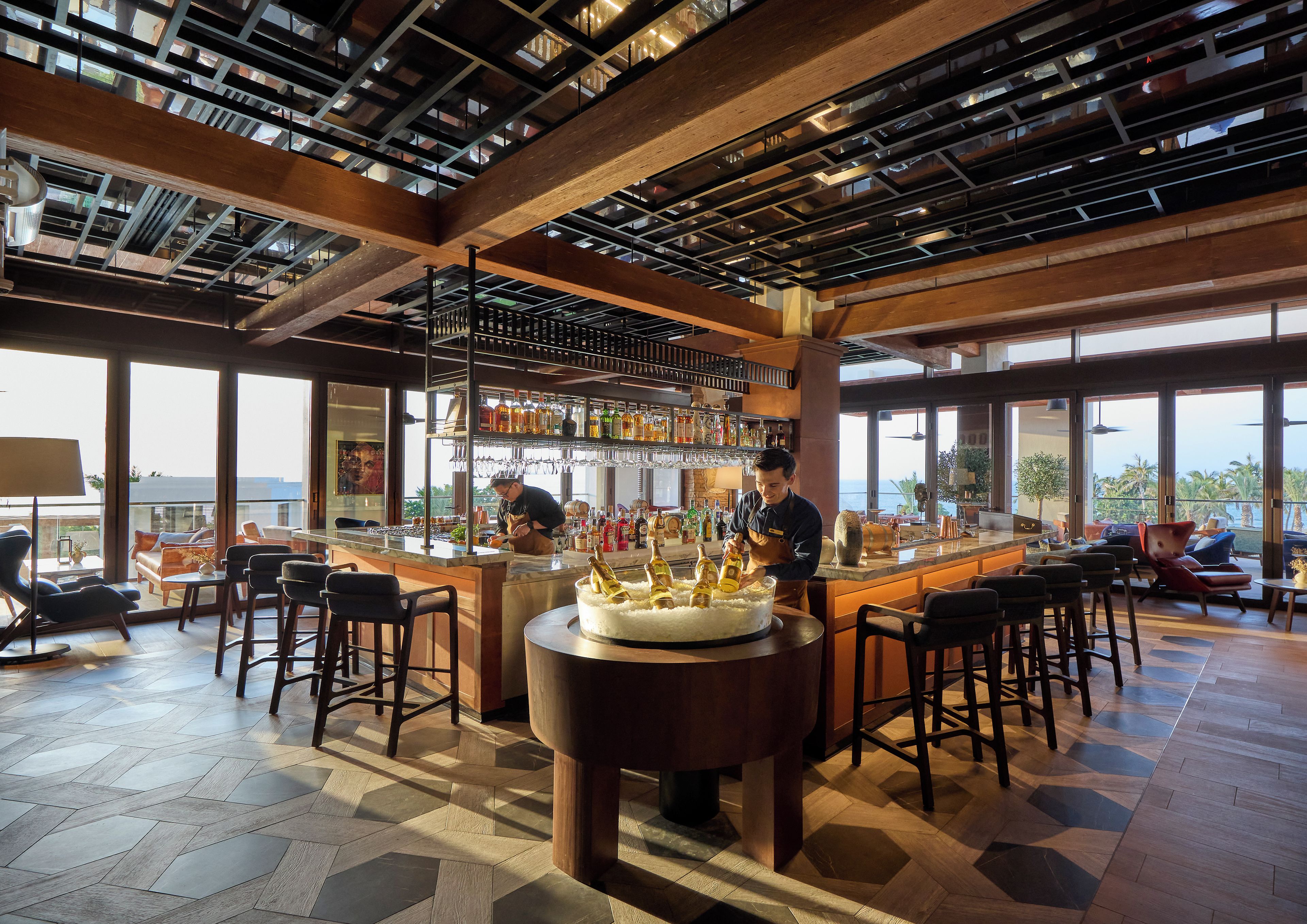Zona de bar con un barman, un pastel grande sobre una mesa y vistas al océano.