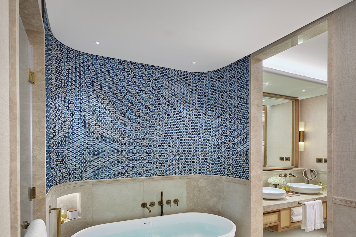 A modern bathroom with a freestanding bathtub, a large mirror, and a tiled wall.
