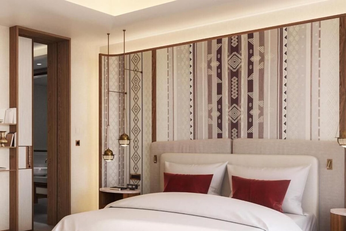 A modern hotel room with a large bed, a bedside table, a mirror, and a patterned wall.