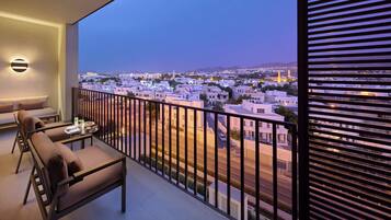 Un balcón con sofá y sillones, con vistas a un paisaje urbano que incluye edificios y una mezquita.