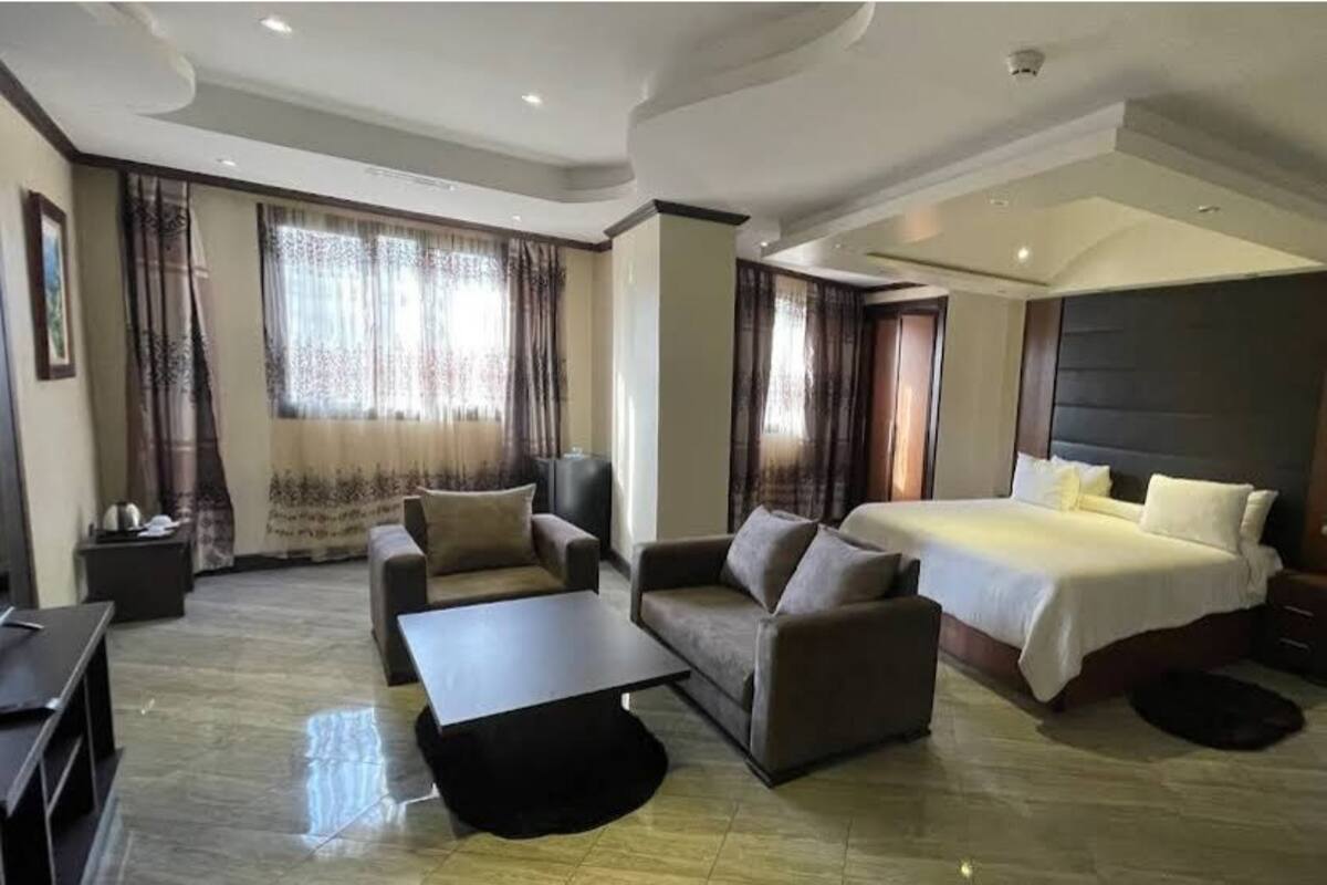 A hotel room with a bed, a sofa, a coffee table, a desk, and a chair.