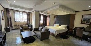 Relax in a spacious room with a large bed, sofa, and desk, offering a comfortable seating area and a view from the large window.