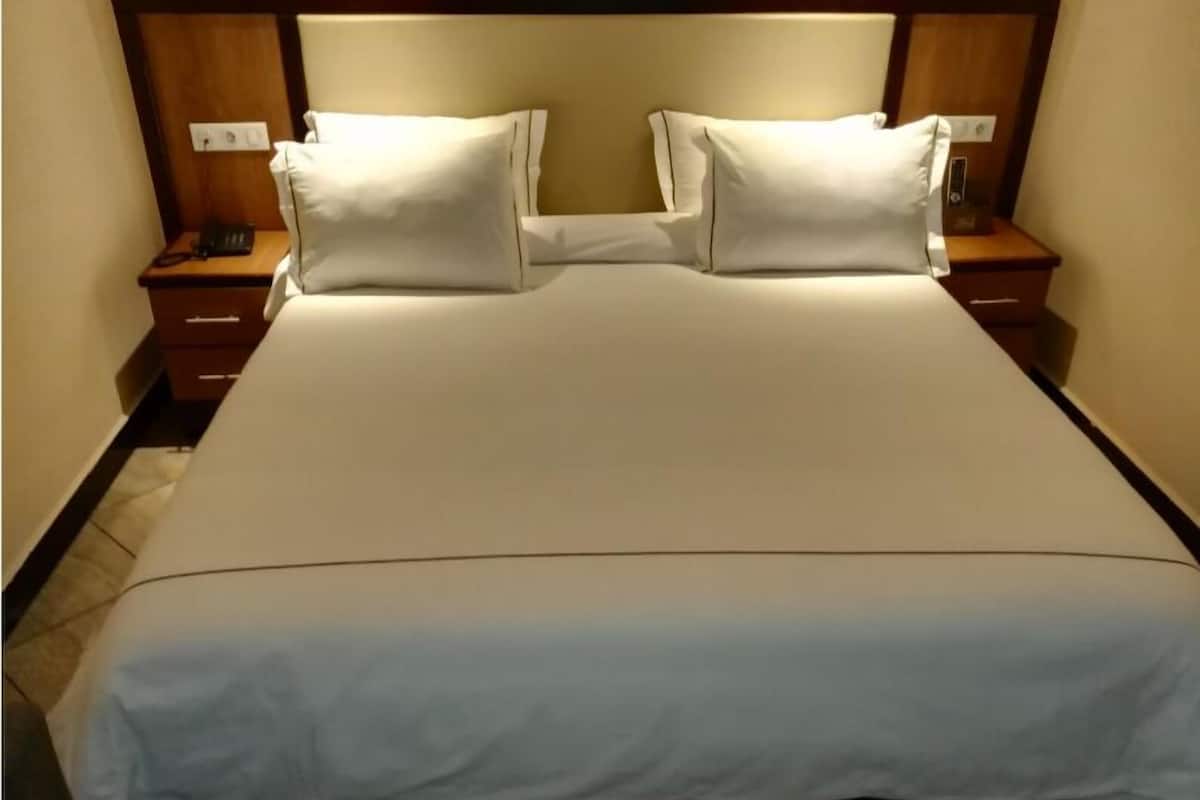 A neatly made bed with white bedding and two pillows, flanked by wooden nightstands with a telephone and a power outlet.