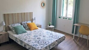 A bedroom with a bed, bedside tables, a small round table, a chair, a window with curtains, and a wall-mounted decoration. - 10 mn à Pieds Vélodrome - T2 Marseille 09 (Marseille)