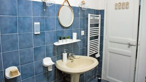 A bathroom with blue tiles, a sink, a mirror, a towel rack, and a door with a sign. - 10 mn à Pieds Vélodrome - T2 Marseille 09 (Marseille)