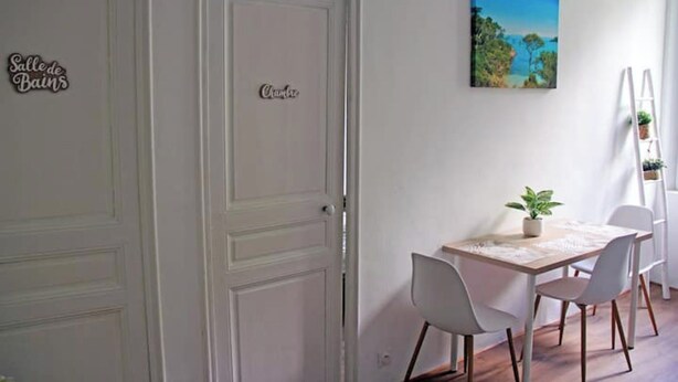 A dining area with a table and chairs, a painting on the wall, and a door with a sign. - 10 mn à Pieds Vélodrome - T2 Marseille 09 (Marseille)