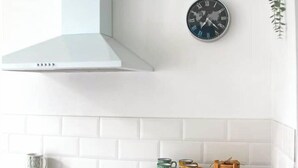A kitchen with a microwave, a clock, and a white tiled backsplash. - 10 mn à Pieds Vélodrome - T2 Marseille 09 (Marseille)