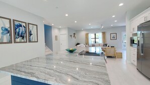 A modern kitchen with a marble countertop, a built-in refrigerator, and a dining area with a sofa and a coffee table. - Oceanview Beach Home, Private Heated Pool, 5 Star Amenities, Steps to Beach (Indian Rocks Beach)