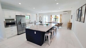 A modern kitchen with a central island, stainless steel appliances, and a dining area with natural light. - Oceanview Beach Home, Private Heated Pool, 5 Star Amenities, Steps to Beach (Indian Rocks Beach)