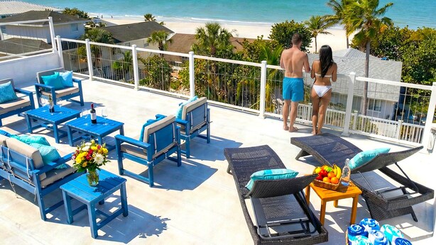 A rooftop terrace with blue furniture, a wicker table with fruit, and a view of the beach and ocean. - Oceanview Beach Home, Private Heated Pool, 5 Star Amenities, Steps to Beach (Indian Rocks Beach)