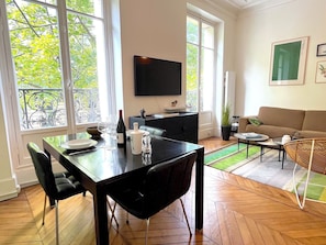 En moderne stue med spiseområde, store vinduer, et fladskærms-tv og en sofa.