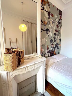 Een slaapkamer met een bed, een spiegel, een openhaard en een muur met bladmotief.