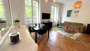 A modern living room with a dining area, large windows, and a flat-screen TV.