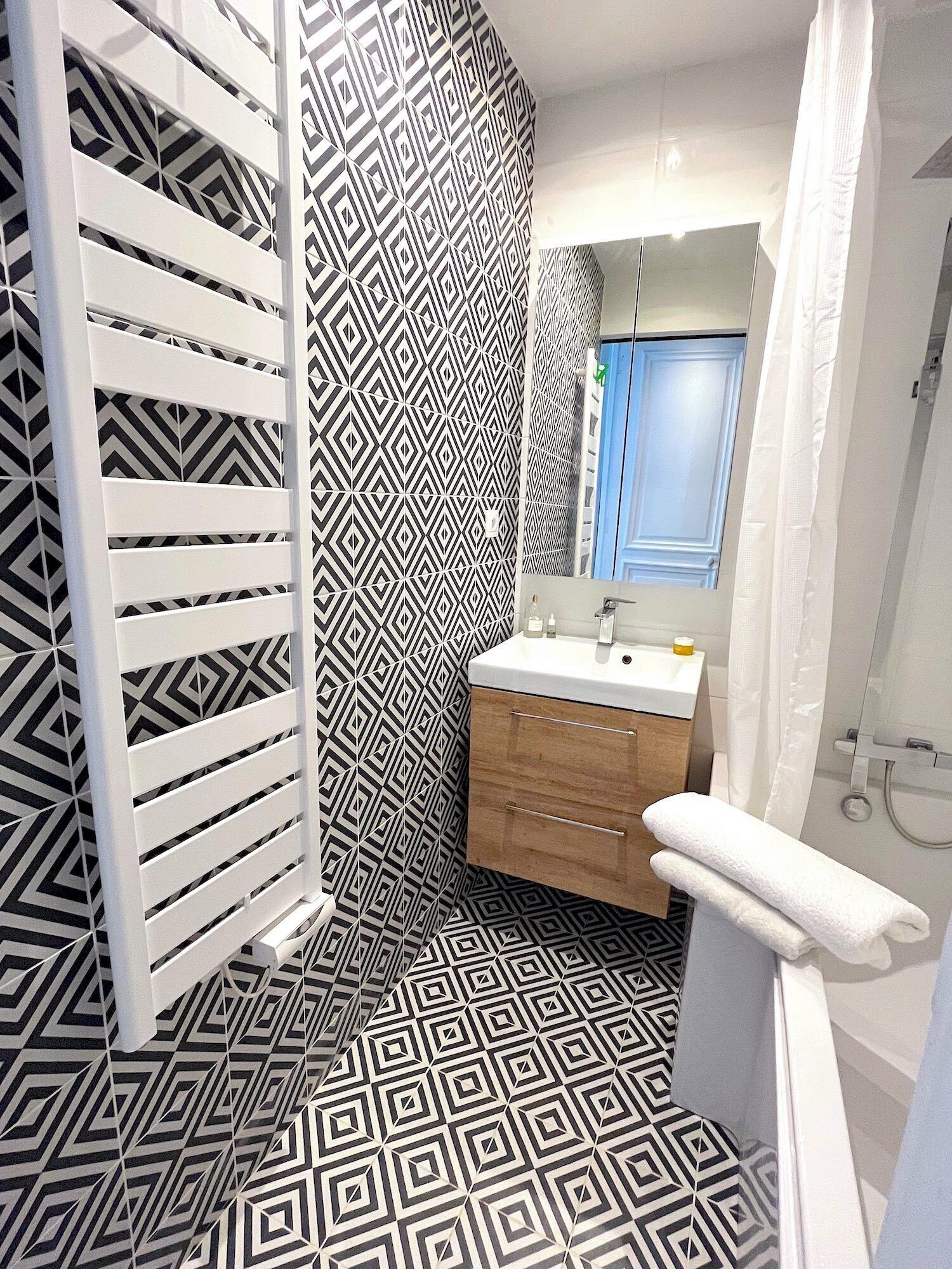 Een badkamer met een vloer met geometrisch patroon, een witte wastafel met een spiegel erboven en een houten kast.