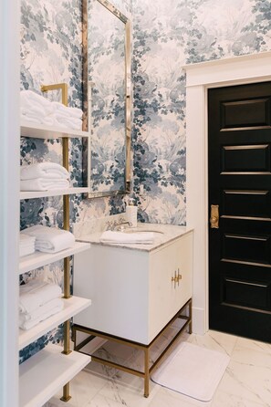 A bathroom with a white vanity, gold fixtures, and a black door.