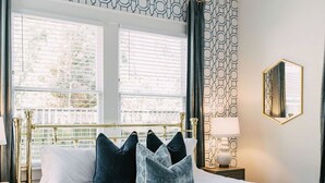 A neatly arranged bedroom with a large bed, a bedside table, a lamp, and a window with blinds. - Midtown Manor by Pettigrew Adventures (Memphis)