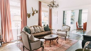 A cozy living room with a brown sofa, two armchairs, a coffee table, and a chandelier. - Midtown Manor by Pettigrew Adventures (Memphis)