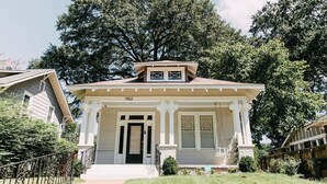 A two-story house with a front porch, a garage, and a large tree in the background. - Midtown Manor by Pettigrew Adventures (Memphis)