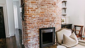 A room with a brick fireplace, a white sofa, and a small round table. - Midtown Manor by Pettigrew Adventures (Memphis)
