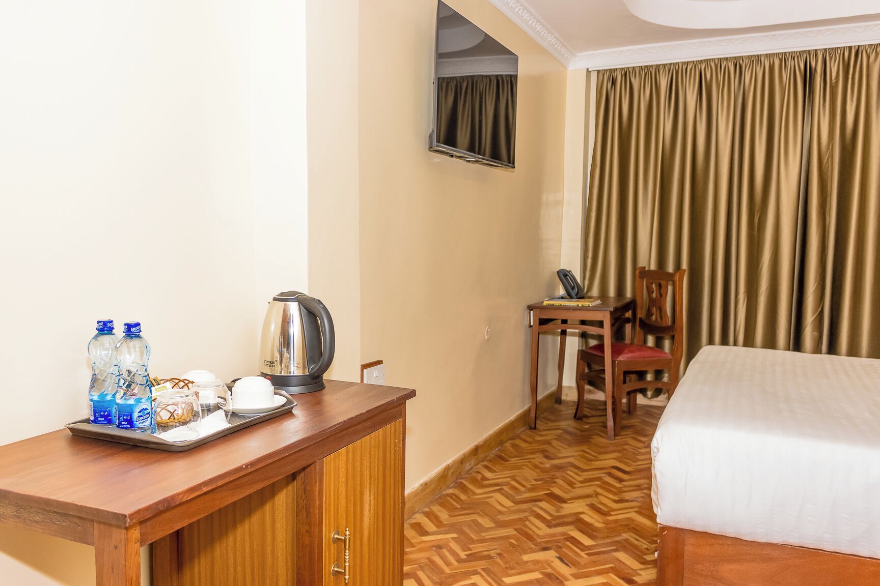 Une chambre d’hôtel avec un lit, un bureau en bois, une bouilloire, une chaise et un téléviseur fixé au mur.