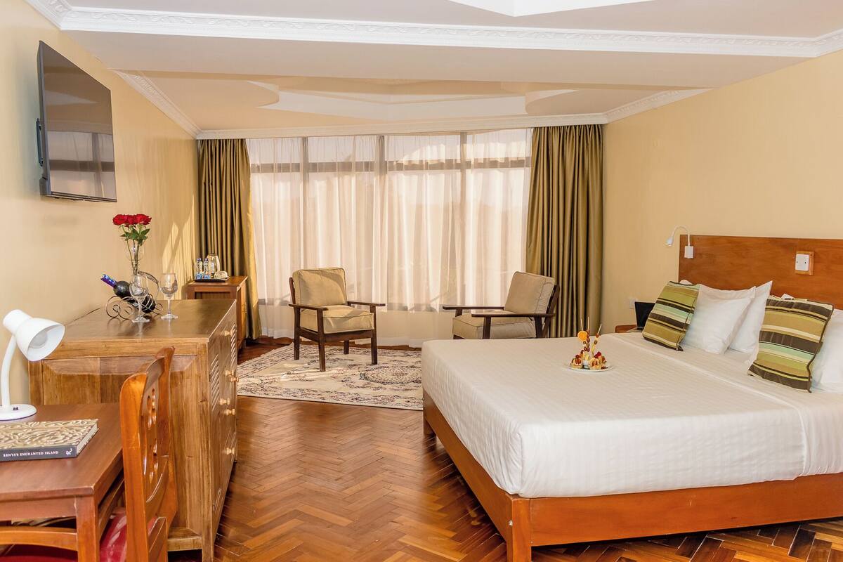 Una habitación de hotel con cama, escritorio, silla, televisión y ventana con cortinas.
